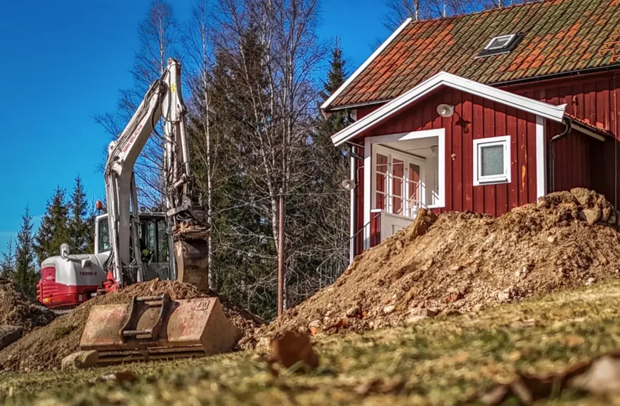 Röd stuga med grävmaskin framför